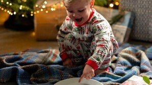 Un enfant assis sur une couverture devant un sapin de Noël illuminé.