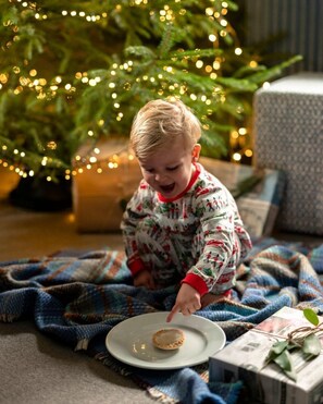 Ein Kind sitzt auf einer Decke vor einem mit Lichtern geschmückten Weihnachtsbaum.