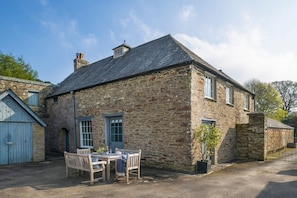 A stone building with a gravel driveway, a wooden table and chairs, and a potted plant.
