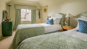 Une chambre avec deux lits, une fenêtre avec des rideaux, une table de chevet avec une lampe et une horloge fixée au mur.