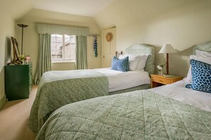Ein Zimmer mit zwei Betten, einem Vorhangfenster, einem Nachttisch mit Lampe und einer Wanduhr.