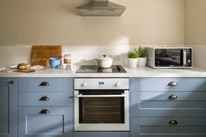 A kitchen with a microwave, oven, and countertop with various items. - Lostwithiel Stable House (Boconnoc)