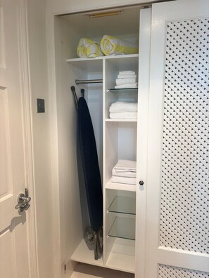 A walk-in closet with shelves for folded towels, a hanging rack for a dark garment, and a door with a patterned glass panel. - Stylish 2BR Condo at Cap Cove (Gros Islet)
