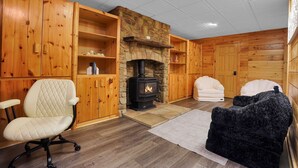 A cozy room with a fireplace, wooden walls, a cushioned chair, and a sofa. - Triple Trac Lodge, upscale retreat in the countryside with 7 Bedrooms, hot tub, game room, and so much more. Plenty of fun for everyone! (East Waterford)