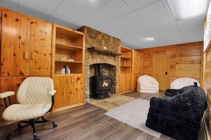 A cozy room with a fireplace, wooden walls, a cushioned chair, and a sofa.
