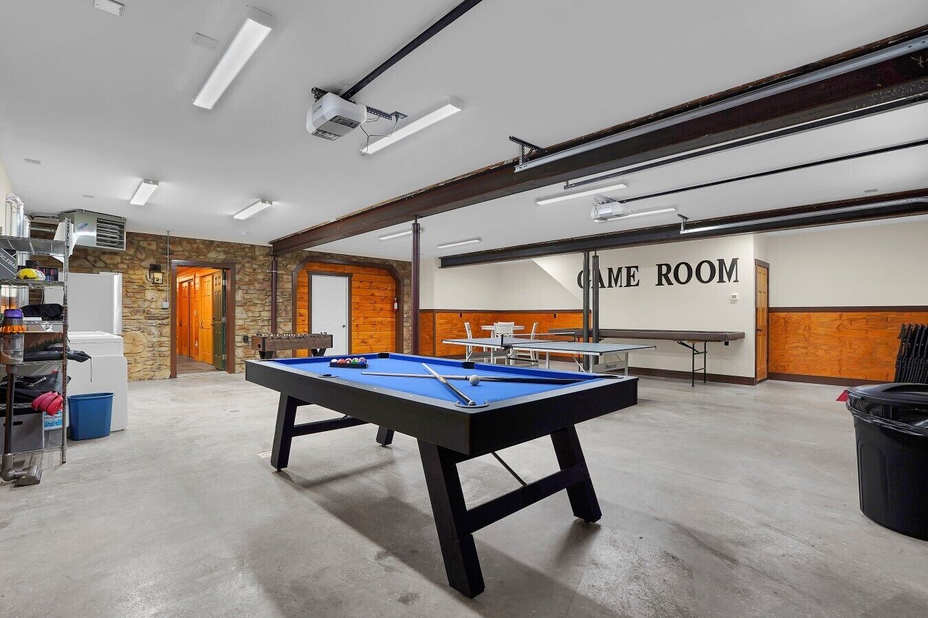 A pool table in a room with a wooden wall and a door labeled 'GAME ROOM'.