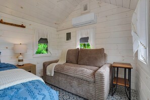 A room with a bed, a sofa, a small table, and an air conditioning unit. - Triple Trac Lodge, upscale retreat in the countryside with 7 Bedrooms, hot tub, game room, and so much more. Plenty of fun for everyone! (East Waterford)
