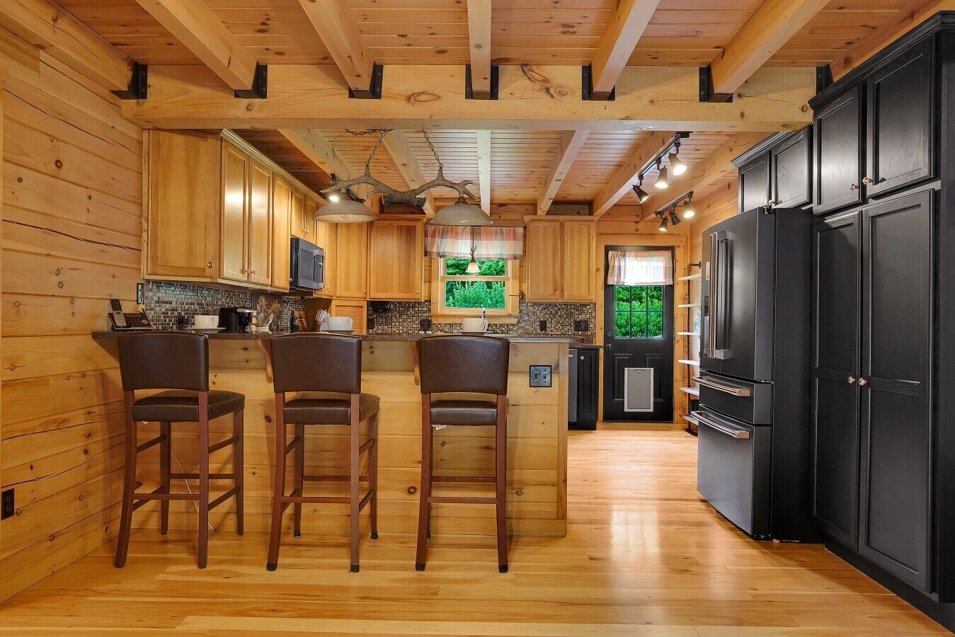 A kitchen with wooden walls, a black refrigerator, and a tiled backsplash.