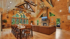 A log cabin interior with a dining area, fireplace, and large windows. - Triple Trac Lodge, upscale retreat in the countryside with 7 Bedrooms, hot tub, game room, and so much more. Plenty of fun for everyone! (East Waterford)