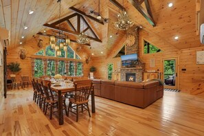 A log cabin interior with a dining area, fireplace, and large windows.