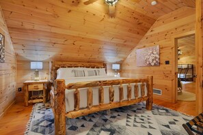 A wooden cabin bedroom with a bed, bedside tables, and a ceiling fan.
