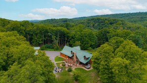 A lodge with a green roof, surrounded by dense forest, and a patio area with outdoor seating. - Triple Trac Lodge, upscale retreat in the countryside with 7 Bedrooms, hot tub, game room, and so much more. Plenty of fun for everyone! (East Waterford)