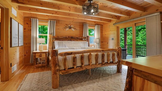 A wooden cabin bedroom with a large bed, a wooden headboard, a ceiling fan, and a view of greenery outside. - Triple Trac Lodge, upscale retreat in the countryside with 7 Bedrooms, hot tub, game room, and so much more. Plenty of fun for everyone! (East Waterford)