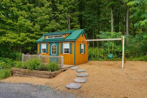A small wooden house with a green roof, surrounded by a forest.