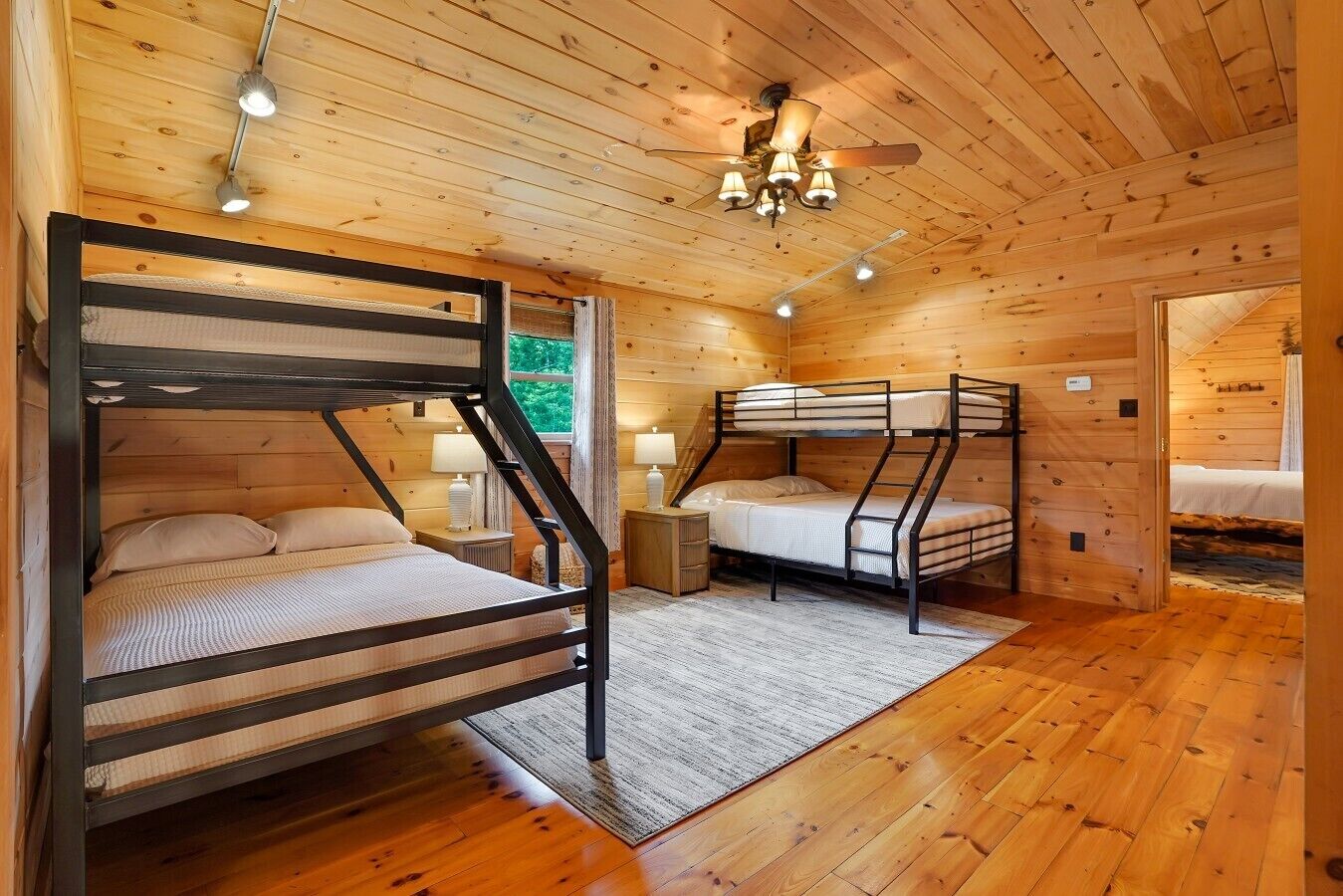 A cabin with two bunk beds, wooden walls, a ceiling fan, and a window.
