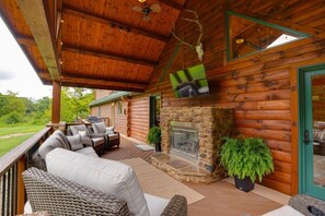 A log cabin with a stone fireplace, outdoor seating, and a television mounted on the wall. - Triple Trac Lodge, upscale retreat in the countryside with 7 Bedrooms, hot tub, game room, and so much more. Plenty of fun for everyone! (East Waterford)