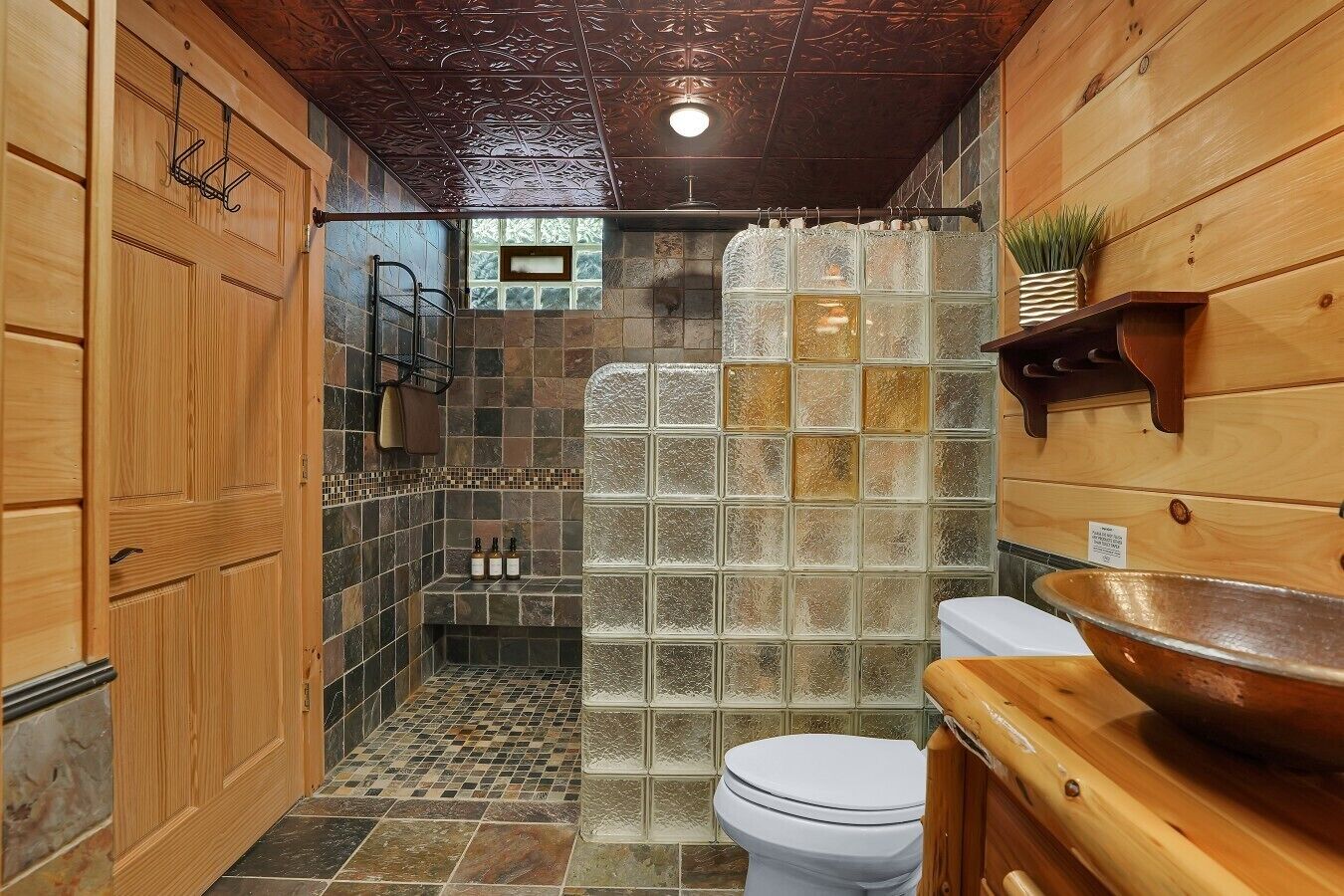 Une salle de bain avec un meuble-lavabo en bois, une cabine de douche en verre et un carrelage au sol.