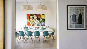 Comedor con una mesa blanca, sillas color turquesa y lámparas de mimbre colgantes.