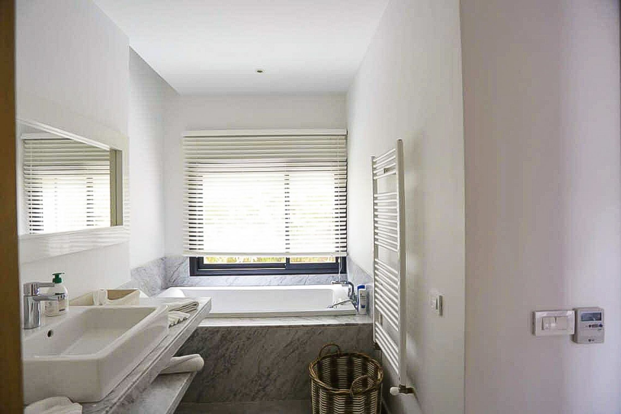 Ein Badezimmer mit Badewanne, großem Spiegel, Waschbecken und einem Fenster mit Jalousien.