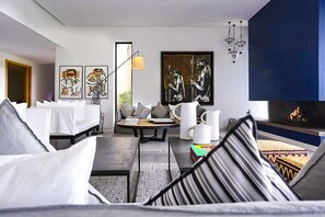 A modern living room with a sofa, a coffee table, and a fireplace. There are framed artworks on the wall and a lamp on the table. - Villa Tallaght - Six Bedroom Villa, Sleeps 12 (Marrakesh)