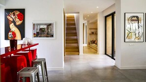 Un interior moderno con una escalera que conduce a un segundo piso, un área de comedor con sillas rojas y obras de arte en las paredes.