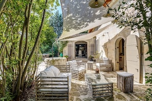 An outdoor seating area with tables and chairs, a stone wall, and a shaded canopy. - Maison Huguette - Five Bedroom Villa, Sleeps 10 (Paradou)