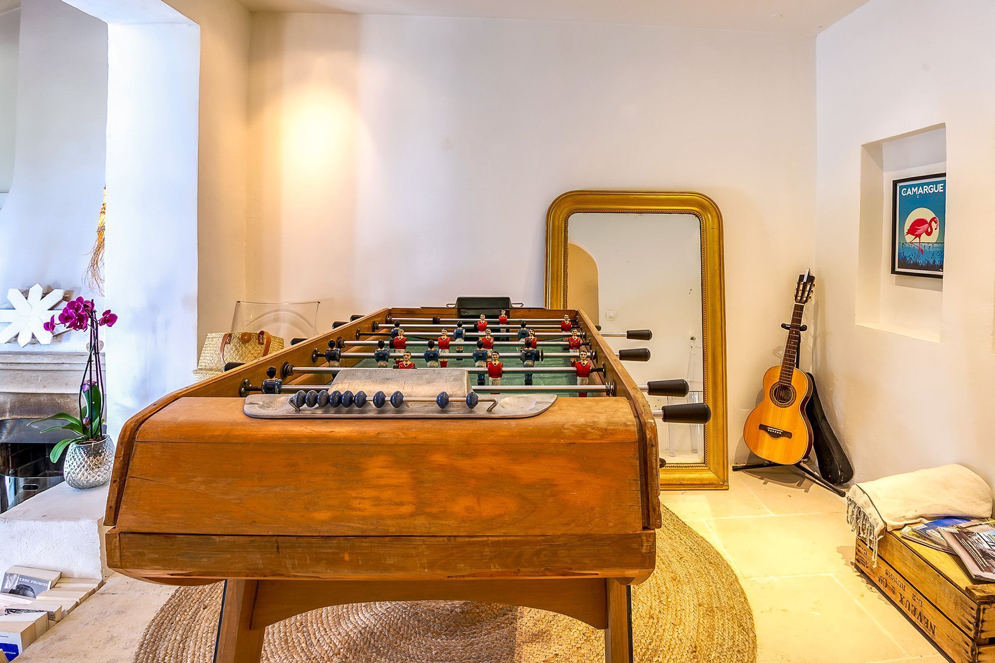 A foosball table in a room with a mirror, a guitar, and a framed picture on the wall.