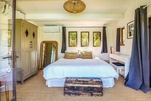 Een slaapkamer met een groot bed, een kledingkast, een airconditioning en een raam met gordijnen.