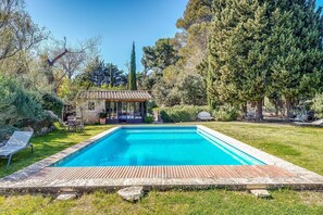 A rectangular swimming pool with a wooden deck in the foreground, surrounded by a well-maintained lawn and various trees. - Maison Huguette - Five Bedroom Villa, Sleeps 10 (Paradou)