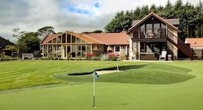 A golf course with a clubhouse featuring a large glass facade, a stone exterior, and a wooden deck.