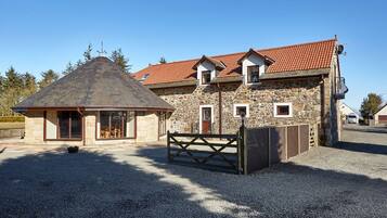 A stone building with a red-tiled roof, a wooden gate, and a gravel driveway.