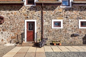 A stone building with a red door, windows, and a small garden area with a bench and a golf bag.