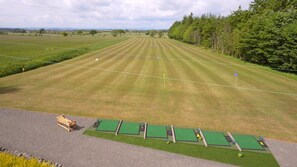 A golf course with a wooden bench, green putting areas, and a clear sky.