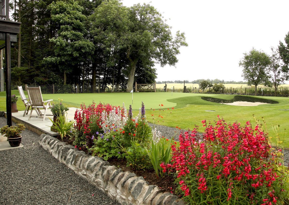 A golf course with a stone border, chairs, and potted plants.
