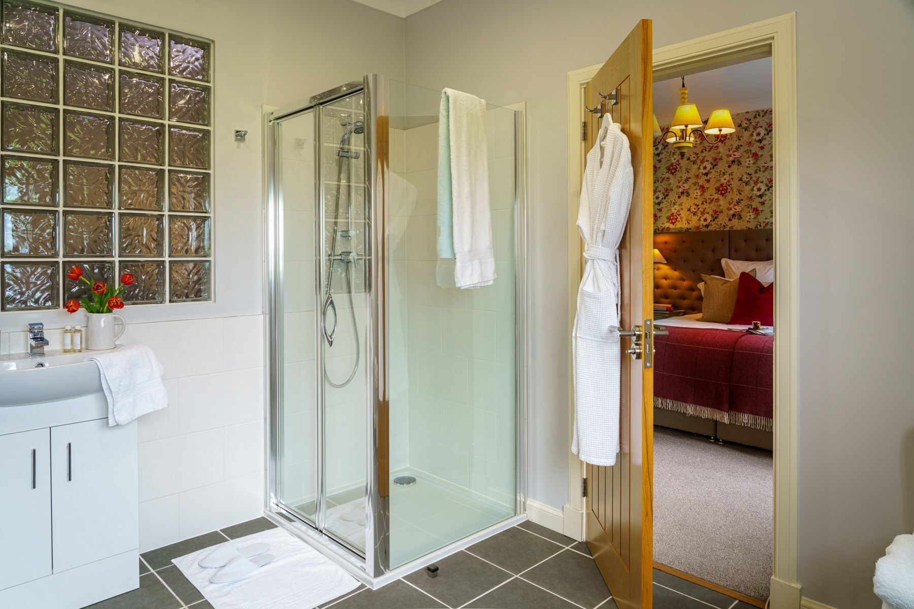 A bathroom with a glass shower enclosure, a white sink, and a mirror with a floral pattern.