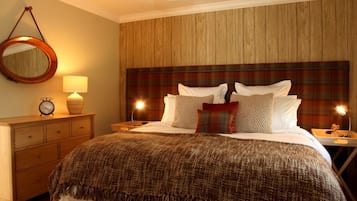 A neatly made bed with a plaid headboard, a bedside lamp, and a wooden nightstand with a clock.