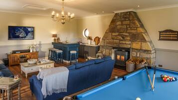 A living room with a pool table, a stone fireplace, a blue sofa, and a chandelier.
