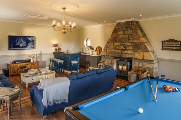 A living room with a pool table, a stone fireplace, a blue sofa, and a chandelier.