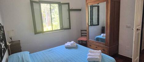 A bedroom with a bed, a bedside table, a chair, a wooden cabinet with a mirror, and a window.