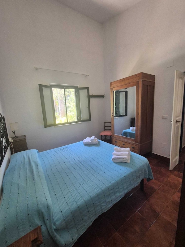 A bedroom with a bed, a bedside table, a chair, a wooden cabinet with a mirror, and a window.