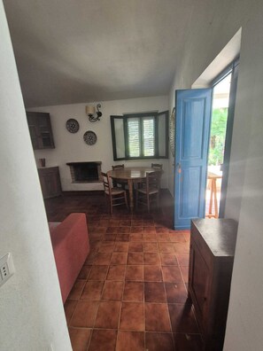 A dining area with a table and chairs, a fireplace, and a blue door leading outside. - A Wonderful Villa Surrounded by Lush Greenery, Peacefully Located Near the Beach (Calabria)