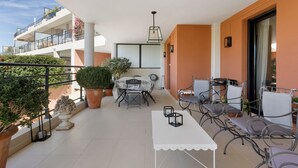 Un balcón con mesa y sillas, plantas en macetas y vista del exterior del edificio.