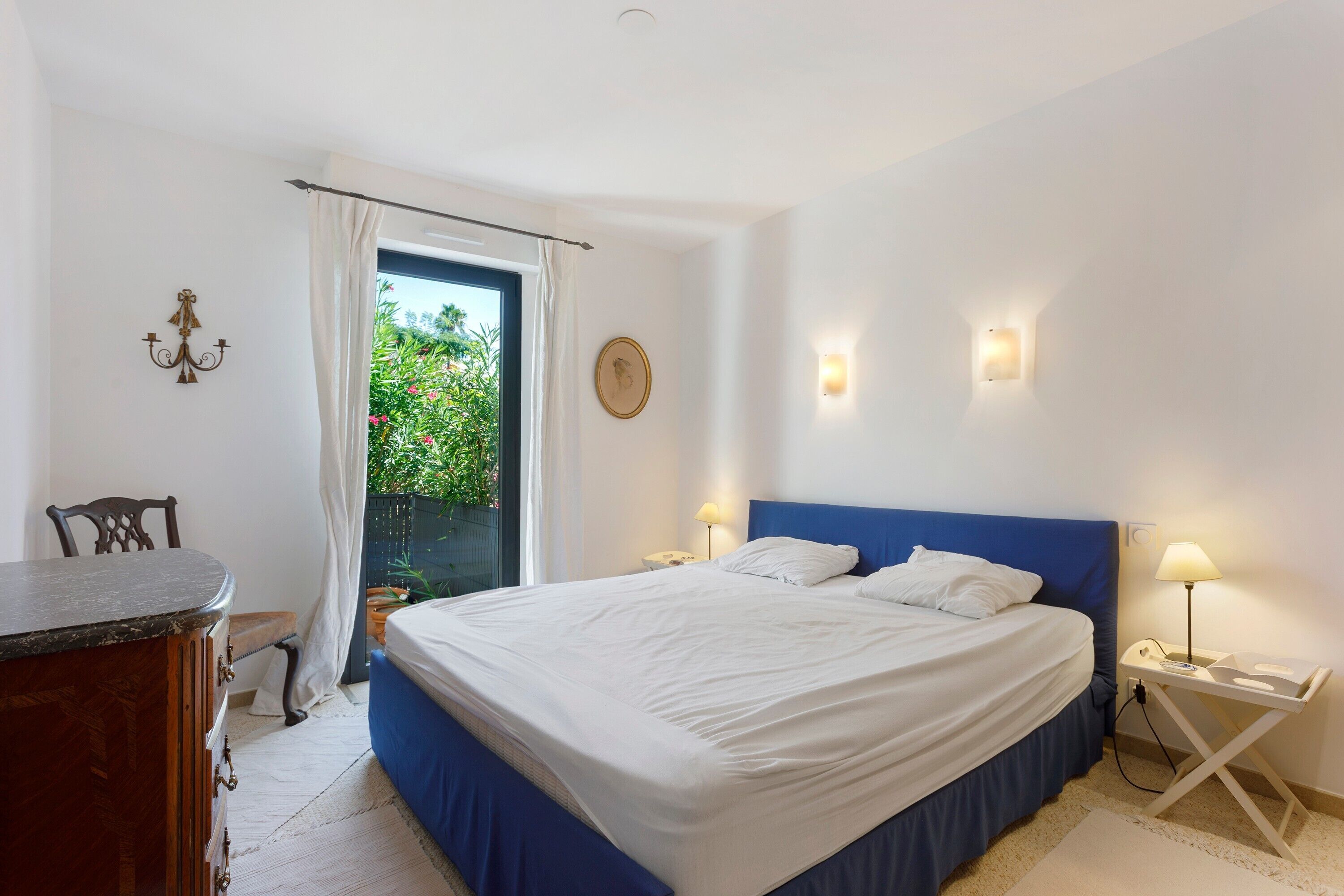 A bedroom with a bed, bedside tables, a chair, a desk, and a window with curtains.