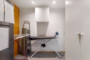 Ein kleines Zimmer mit Wandbügelecke, einer kleinen Bügeleinrichtung und einer abschließbaren Tür.