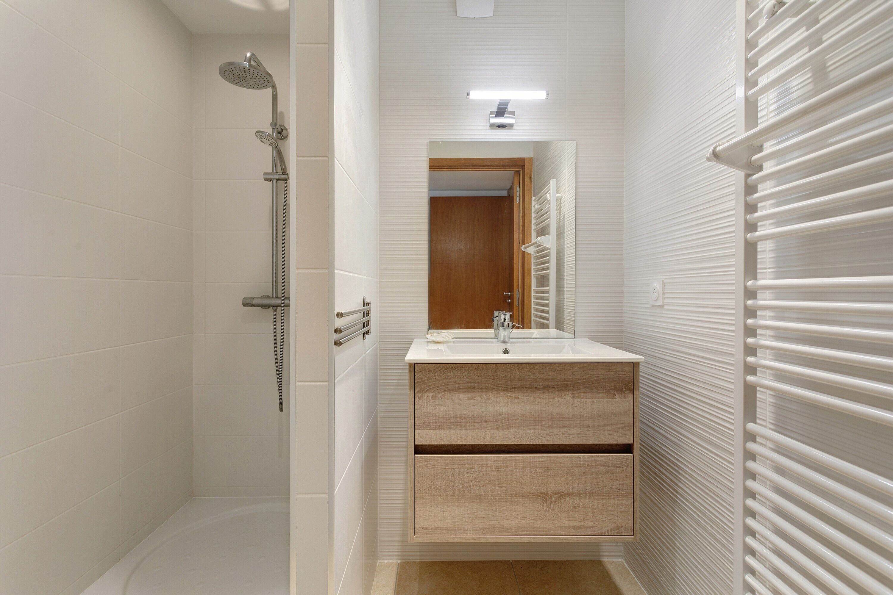 Ett modernt badrum med dusch, handfat med spegel och handdukshängare.
