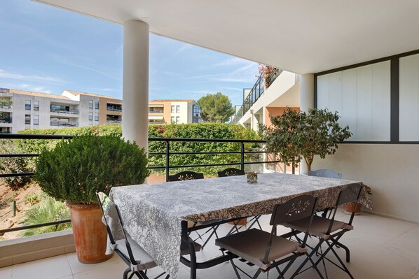A balcony with a table and chairs, a potted plant, and a view of buildings and trees. - “Saint Raphael De Luxe” Apartment with Shared Pool and Private Terrace (Saint-Raphaël)