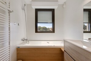 A modern bathroom with a bathtub, a shower, and a window with blinds. - “Saint Raphael De Luxe” Apartment with Shared Pool and Private Terrace (Saint-Raphaël)