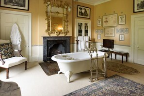 A classic room with a freestanding bathtub, a fireplace, a large mirror, and a collection of framed pictures on the wall.