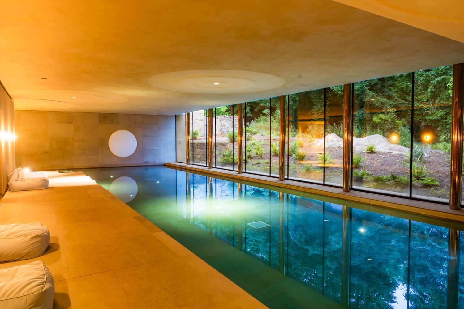 Ein moderner, überdachter Schwimmbereich mit freiem Blick ins Freie, einer Lounge mit Kissen und einer Steinwand.
