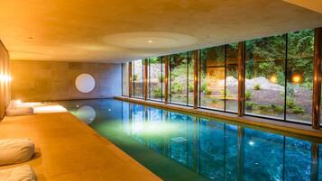 Ein moderner, überdachter Schwimmbereich mit freiem Blick ins Freie, einer Lounge mit Kissen und einer Steinwand.